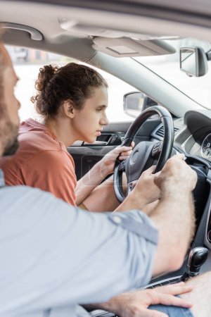 bearded father pointing at speedometer while teaching teenage son how to drive car 