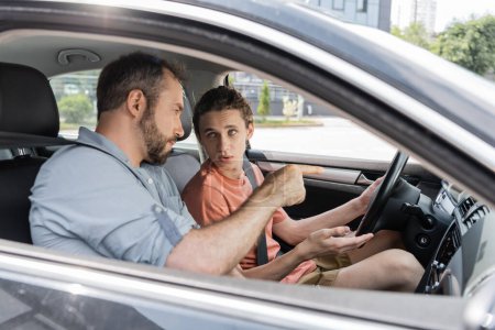 barbudo padre hablando con hijo adolescente mientras le enseña a conducir coche 