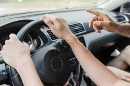 cropped view of father pointing away with finger while teenage son driving car 