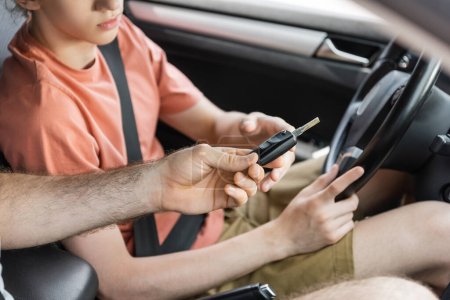 cropped view of father giving car key to teenage son sitting next to steering wheel  