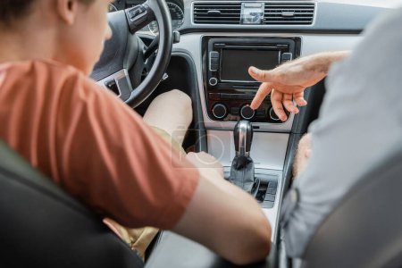 father pointing at changing gear handle while teaching son how to drive car 