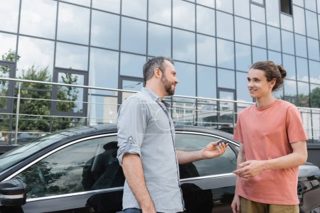 Glücklicher bärtiger Mann übergibt Autoschlüssel an Teenager-Sohn in der Nähe von Auto 
