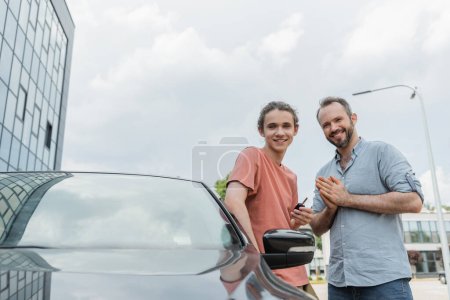 Glücklicher Vater und Teenager-Sohn stehen zusammen neben modernem Auto 