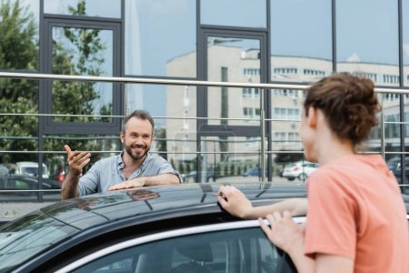 Glücklicher Vater schaut Teenager-Sohn beim Zusammenstehen in der Nähe moderner Autos an 