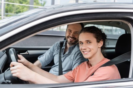 fröhlicher Vater und Teenager-Sohn blicken in die Kamera, während sie zusammen im Auto sitzen 