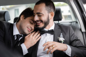 Smiling bearded man in elegant suit with boutonniere sitting near young brunette groom with closed eyes in car after wedding celebration while going on honeymoon  mug #654380358