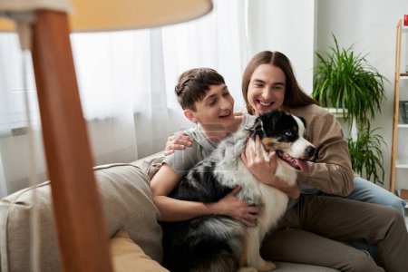 Smiling lgbt couple in casual clothes petting friendly Australian shepherd dog while sitting on couch near blurred floor lamp in modern living room at home 