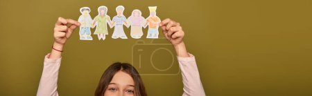 Cropped view of preteen kid holding drawn paper characters above head during child protection day celebration on khaki background, banner 