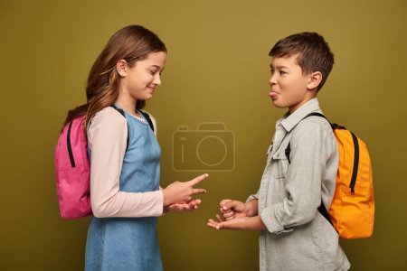 Photo for Funny multiethnic kids with backpacks smiling and playing rock paper scissors game during international children day celebration on khaki background - Royalty Free Image