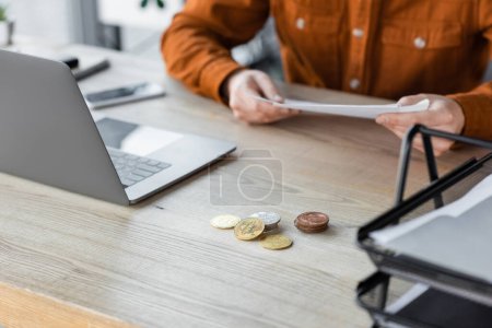 Photo for KYIV, UKRAINE - OCTOBER 18, 2022: cropped view of businessman in stylish shirt sitting with documents next to smartphone, laptop, silver and golden bitcoins on work desk in modern office - Royalty Free Image