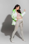 full length of future mother in crop top, stylish blazer, leggings and beads belt standing and holding hand on waist on grey background, expectation, maternity fashion concept Poster #656081666