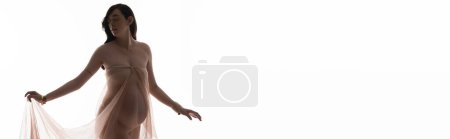 graceful and pregnant woman in golden bracelets holding soft chiffon cloth while posing isolated on white background, maternity fashion concept, banner, expectation, future mother with belly