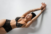 top view of young, tattooed and desirable woman with sexy body, wearing black bra with pearl beads while laying on grey background, art of seduction, erotic photography magic mug #658314654