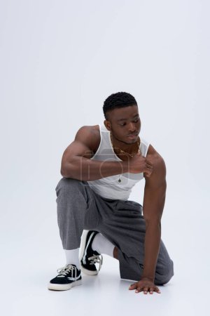Photo for Full length of muscular young african american man in tank top and pants touching golden necklace and posing confidently in stylish and trendy outfit on grey background, good looking - Royalty Free Image