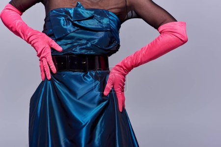 Ausgeschnittene Ansicht einer trendigen jungen Frau in Cocktailkleid und rosa Handschuhen, die die Hüften berührt und isoliert auf grau steht, Modekonzept der modernen Generation z, Details, Gürtel, feminin