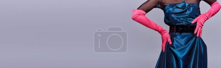 Téléchargez les photos : Cropped view of trendy young woman in cocktail dress and pink gloves touching hip and posing isolated on grey, modern generation z fashion concept, details, belt, feminine, banner - en image libre de droit