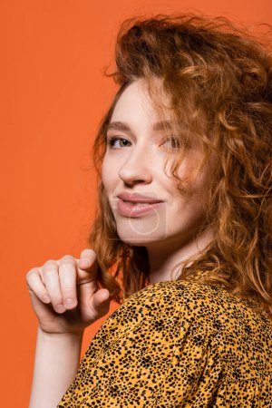 Photo for Portrait of young red haired model in yellow blouse with abstract print looking at camera and standing isolated on orange, stylish casual outfit and summer vibes concept, Youth Culture - Royalty Free Image