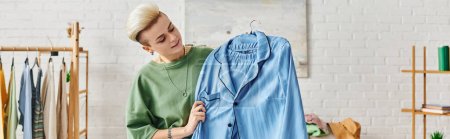 clothing sorting, home decluttering, tattooed woman with trendy hairstyle holding blue pajamas near rack with garments on hangers, sustainable living and mindful consumerism concept, banner