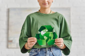 eco-conscious lifestyle, partial view of smiling tattooed woman in casual clothes holding green recycling symbol around globe at home, sustainable living and environmental awareness concept mug #661656936