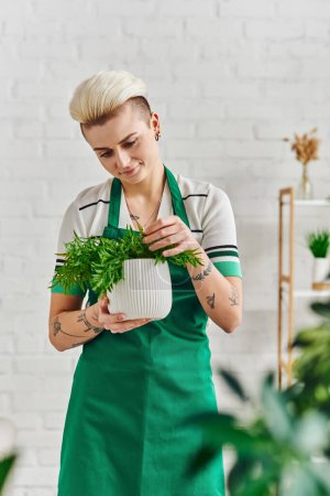 plant care, indoor gardening, smiling tattooed woman in green apron touching natural potted plant while standing in modern living room, sustainable home decor and green living concept