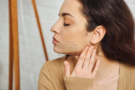 Photo for Side view of young brunette woman in brown jumper massaging face for lymphatic system support and drainage at home, self-care ritual and holistic healing concept, tension relief - Royalty Free Image
