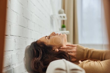 Widok z boku zrelaksowany brunetka kobieta w brązowy skoczek masaż węzłów chłonnych na szyi podczas pielęgnacji samoopieki na kanapie w domu, samoopieki rytuał i holistyczne uzdrowienie koncepcji, rozładowanie napięcia