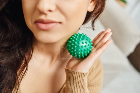Cropped view of blurred young brunette woman massaging neck with manual massage ball at home, lymphatic system support and home-based massage, balancing energy and tension relief