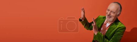 glücklich und trendy alterndes Konzept, aufgeregter grauhaariger und bärtiger älterer Herr im grünen Velours-Blazer mit Stop-Geste und Lachen mit geschlossenen Augen auf rot-orangefarbenem Hintergrund, Banner mit Kopierraum