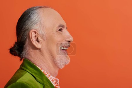 Photo for Profile portrait of charismatic and joyous older model smiling on vibrant orange background, senior man with grey hair and beard, wearing green velour blazer, happy and stylish aging concept - Royalty Free Image
