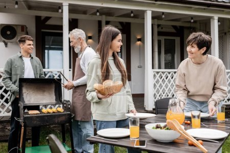 parents day, happy teenage girl helping mother, holding buns, serving table, father and son making bbq, grilling corn, backyard of summer house, suburban life, family bbq party, celebration 