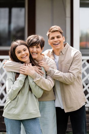 family photo, happy parents day, cheerful teenage girl and young adult son hugging mother on backyard of summer house, family celebration, bonding, moments to remember, modern parenting 