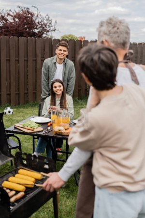 parents day celebration, happy siblings looking at father and mother on blurred background, family bbq, grill party, using smartphone, preparing food on grill bbq, modern parenting 