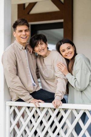 parents day concept, middle aged woman smiling with cheerful daughter and son on porch of summer house, looking at camera, family reunion, bonding, modern parenting, moments to remember 