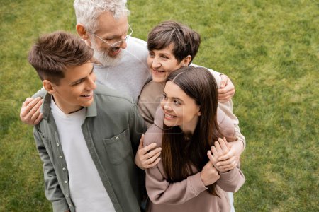 Overhead view of smiling middle aged parents hugging children and looking at each other while celebrating parents day on backyard in june, quality time with parents concept, special occasion