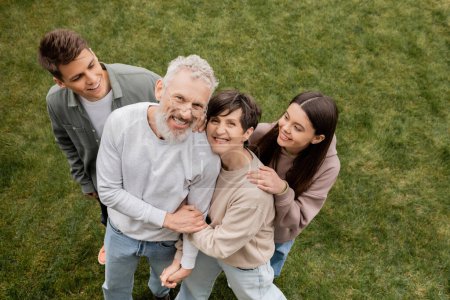 Overhead view of smiling kids hugging middle aged parents looking at camera while celebrating parents and family day at backyard in june, quality time with parents concept 