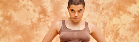 body positivity, curvy and tattooed woman in crop top posing on mottled beige background, looking at camera, representation of body, different body shapes, generation z, youth, banner 