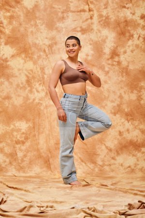 Photo for Body positivity, confident, curvy and happy woman in crop top and jeans posing on mottled beige background, casual attire, self-acceptance, generation z, tattooed, smile, full length, denim fashion - Royalty Free Image