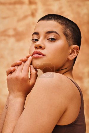 body positivity and confidence, curvy and young woman posing on mottled beige background, short haired, looking at camera, self-acceptance, generation z, tattooed, different shapes, portrait 