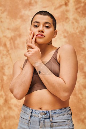 body positivity and confidence, curvy and young woman in crop top and jeans posing on mottled beige background, short haired, self-acceptance, generation z, tattooed, different shapes 