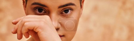 natural look, self-acceptance, young woman with short hair posing on mottled beige background, hand near face, individuality, modern generation z, beauty and skincare, banner