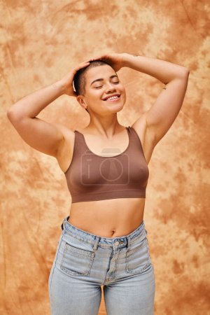 body acceptance, curvy and cheerful woman in crop top posing on mottled beige background, smiling with closed eyes, representation of body, different shapes, generation z, youth, tattooed  