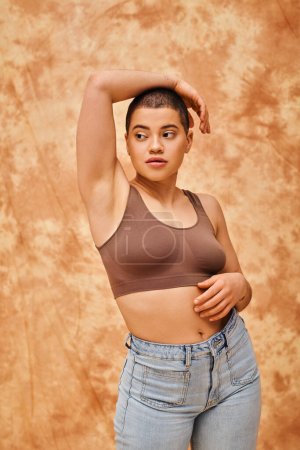 Photo for Body love, curvy young woman in crop top posing with raised hand on mottled beige background, looking away, representation of body, different shapes, generation z, youth, tattooed, relaxed pose - Royalty Free Image