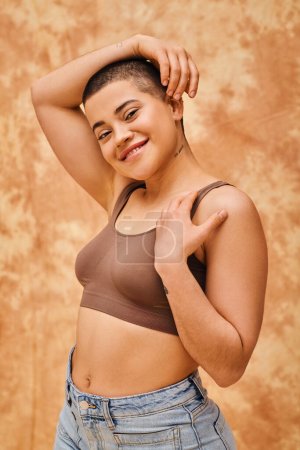 body love, curvy young and happy woman in crop top posing on mottled beige background, looking at camera, representation of body, different shapes, generation z, youth, tattooed, relaxed pose 