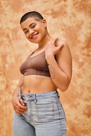 body love, jeans look, curvy and tattooed woman in casual attire standing on mottled beige background, confidence, self-acceptance, generation z, body diversity, pretty and positive 