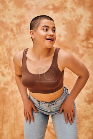 Photo for Body image, jeans look, amazed and tattooed woman in casual attire standing on mottled beige background, confidence, self-acceptance, generation z, body diversity, pretty and short haired model - Royalty Free Image