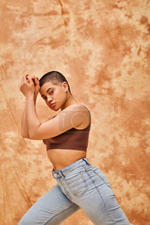 denim fashion, gen z, young curvy woman with tattoo posing on mottled beige background, different shapes, body positivity movement, self-esteem, confidence, short haired model, youth culture 