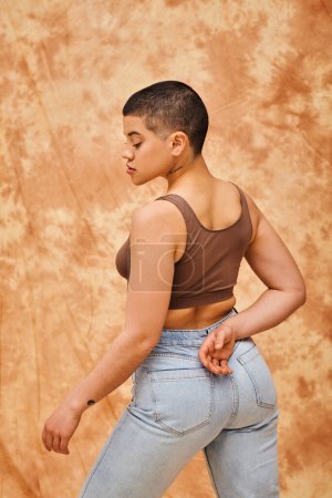 denim fashion, gen z, curvy model with tattoo posing on mottled beige background, different shapes, body positivity movement, self-esteem, confidence, short haired woman, youth culture 