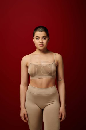 Photo for Body diversity, young tattooed woman in beige underwear posing on red background, body positivity, real people, burgundy, comfortable in skin, curvy model, generation z, self love, looking at camera - Royalty Free Image