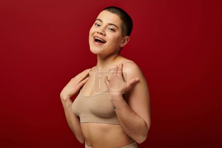 self acceptance, excited and tattooed woman in beige underwear posing on red background, body positivity, curvy fashion, comfortable in skin, self-acceptance, generation z, body diversity, laughter 