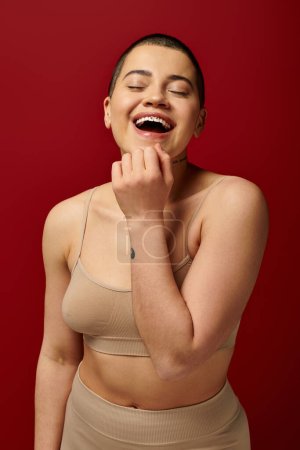 Photo for Self-esteem, excited and tattooed woman in beige underwear posing on red background, body positivity, curvy fashion, comfortable in skin, self-acceptance, generation z, body diversity, laughter - Royalty Free Image